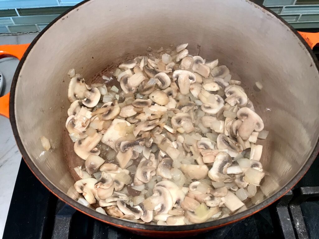 Mushrooms and onions cooking in a dutch oven for Brazilian Chicken Stroganoff.