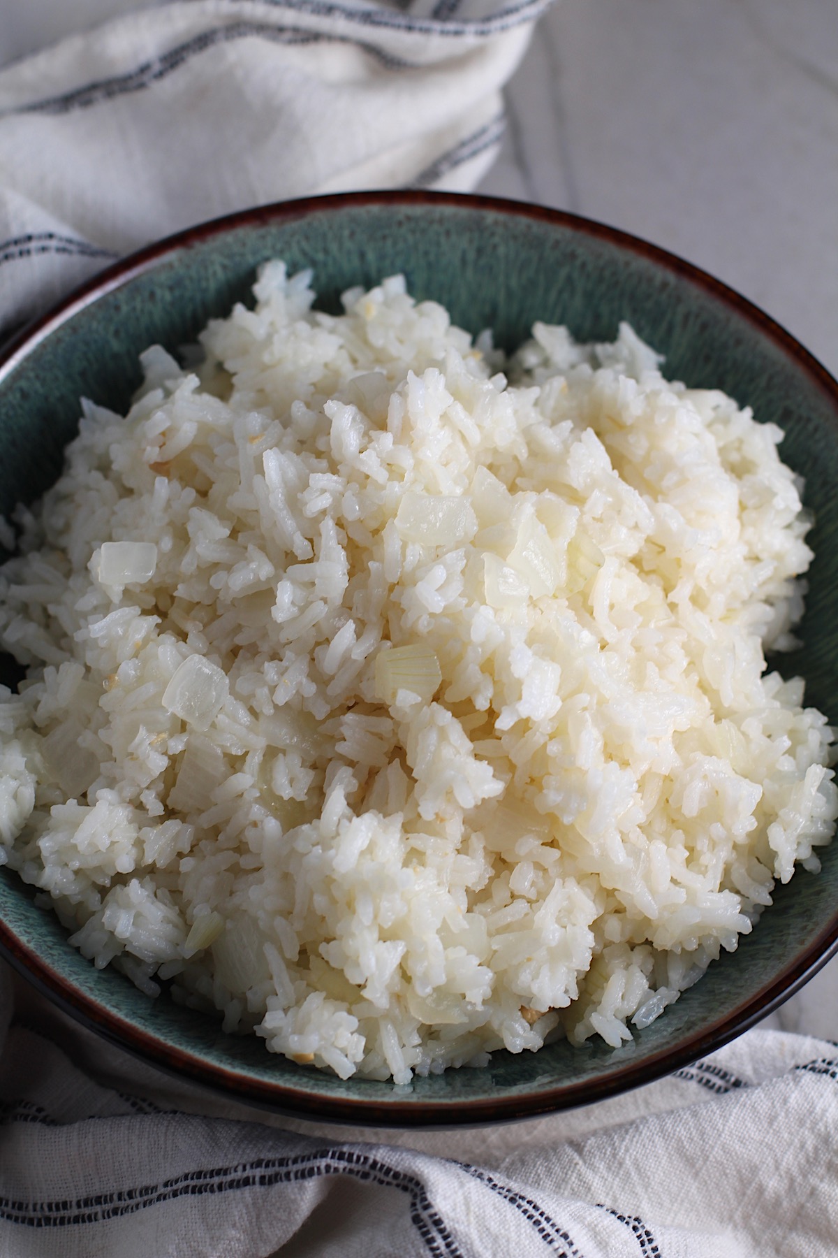 Brazilian Rice in a bowl on counter next to a towel.  It's fluffy white rice flavored with sauteed garlic and onion.  It takes only a couple additional steps and goes with anything!