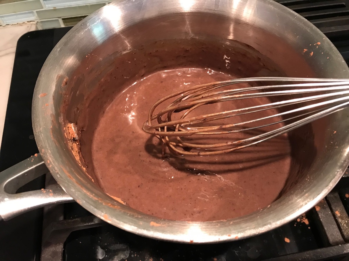 Sweetened evaporated milk and chocolate being whisked in a pot. This Brigadeiro Recipe is based on traditional Brazilian chocolate dessert truffles rolled in sprinkles. You won't believe how easy they are to make!