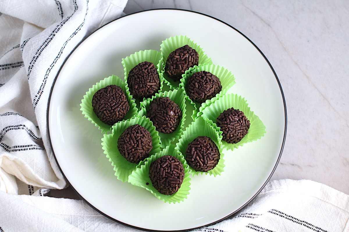 Brigadeiros, Brazilian Chocolate Dessert truffles in green paper on a plate. This Brigadeiro Recipe is based on traditional Brazilian chocolate truffles rolled in sprinkles. You won't believe how easy they are to make!