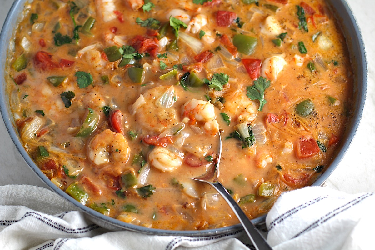 Coconut Shrimp Stew or Moqueca de Camarão, in a pan with a spoon. It's a delicious traditional dish in Brazil. It's a creamy stew with coconut milk and vegetables.
