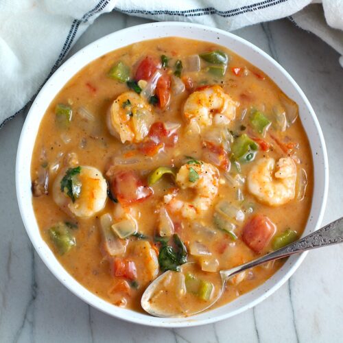 Coconut Shrimp Stew or Moqueca de Camarão, in a bowl with a spoon. It's a delicious traditional dish in Brazil. It's a creamy stew with coconut milk and vegetables.