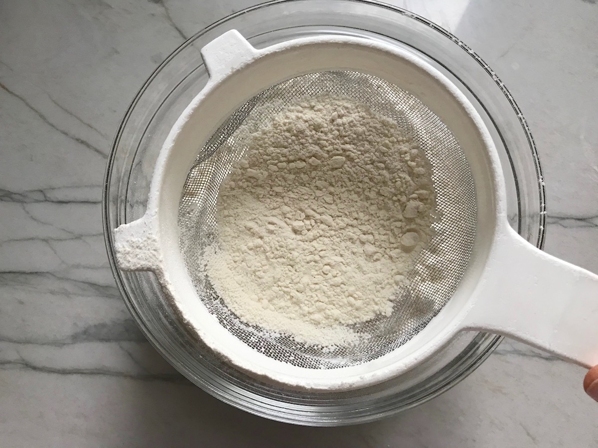 Sifting flour over a bowl for Brazilian Carrot Cake recipe.
