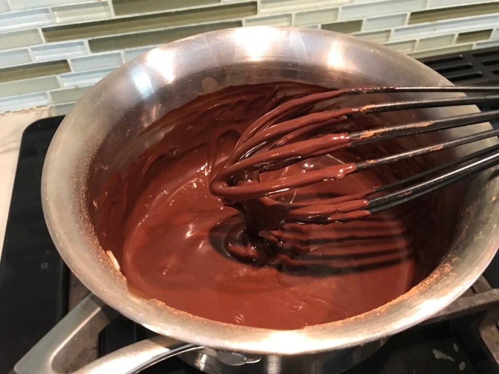 Chocolate sauce topping cooking on a saucepan with whisk for Brazilian Carrot Cake.
