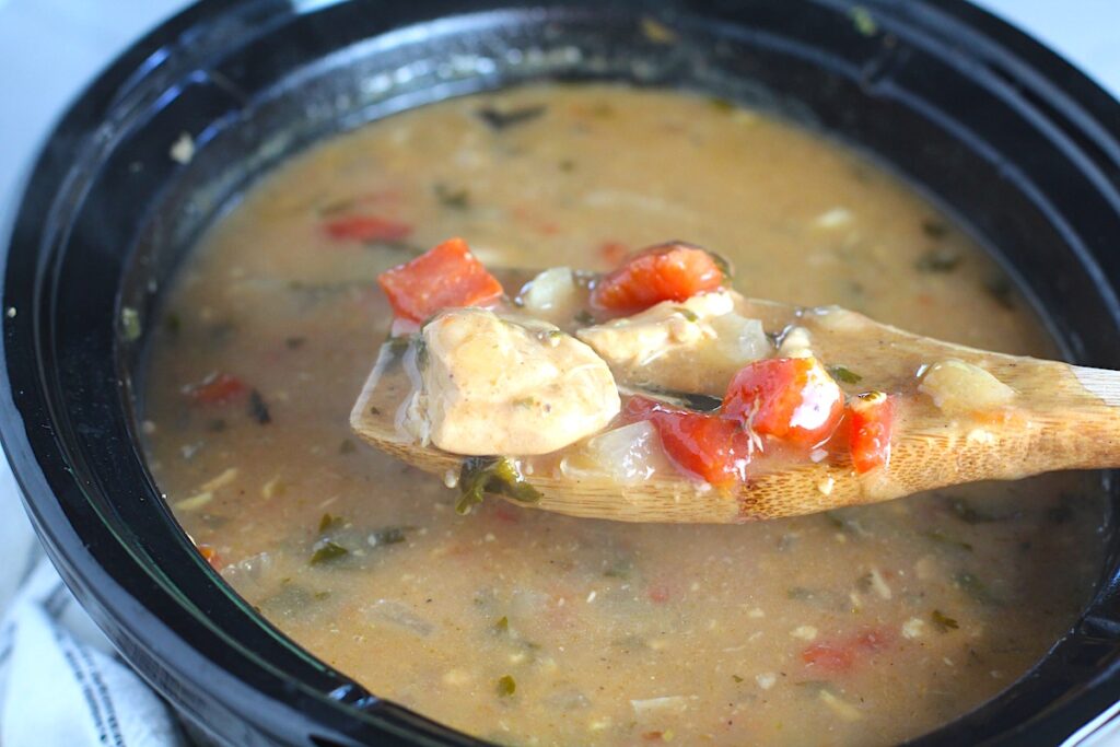 Brazilian Coconut Chicken Stew in a slow cooker with a spoon scooping some up. It's an easy family dinner. It's has chicken thighs, tomatoes, lime, cilantro, and more. Cook in a slow cooker or on the stove!