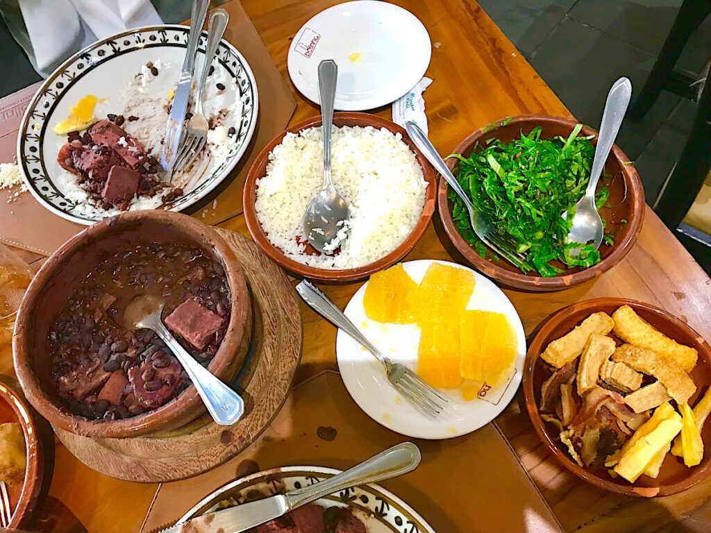Table with feijoada, orange slices, kale, yuka, rice, and other plates from Bolinha restaurant in Sao Paulo, Brazil.