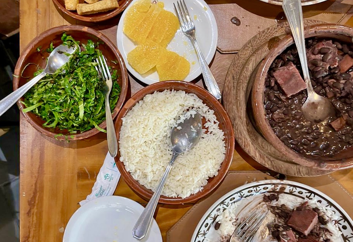 Table with feijoada, orange slices, kale, yuka, rice, and other plates from Bolinha restaurant in Sao Paulo, Brazil.