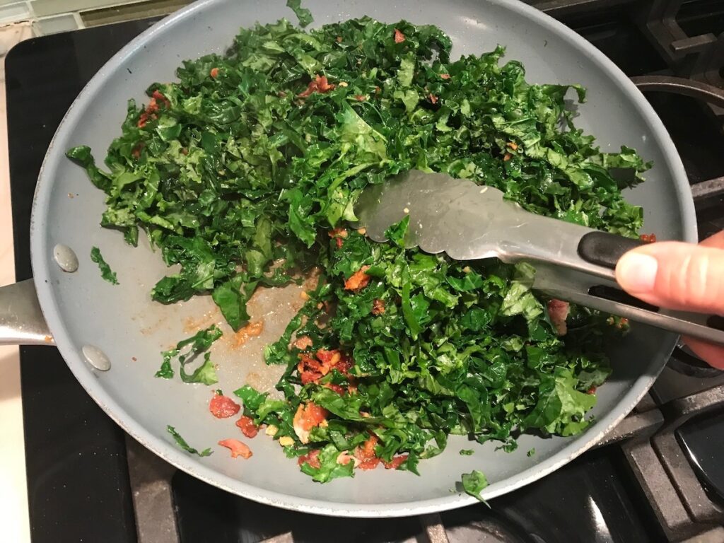Tongs mixing kale and bacon in pan for Kale with Bacon.