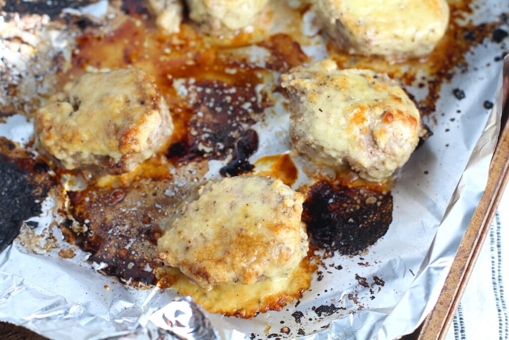 Parmesan Pork Tenderloin pieces on a pan. They are juicy, salty, and slightly cheesy. It's easy to make in the oven so you can enjoy it at home anytime!
