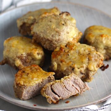 Parmesan Pork Tenderloin pieces on a plate with one cut in half. They are juicy, salty, and slightly cheesy. It's easy to make in the oven so you can enjoy it at home anytime!