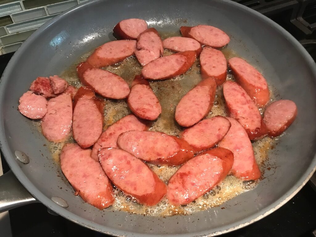 Pre-cooked pork sausage cooking in a frying pan for Feijoada recipe. It is rice and beans Brazilian style with pork sausages, beef, and more.