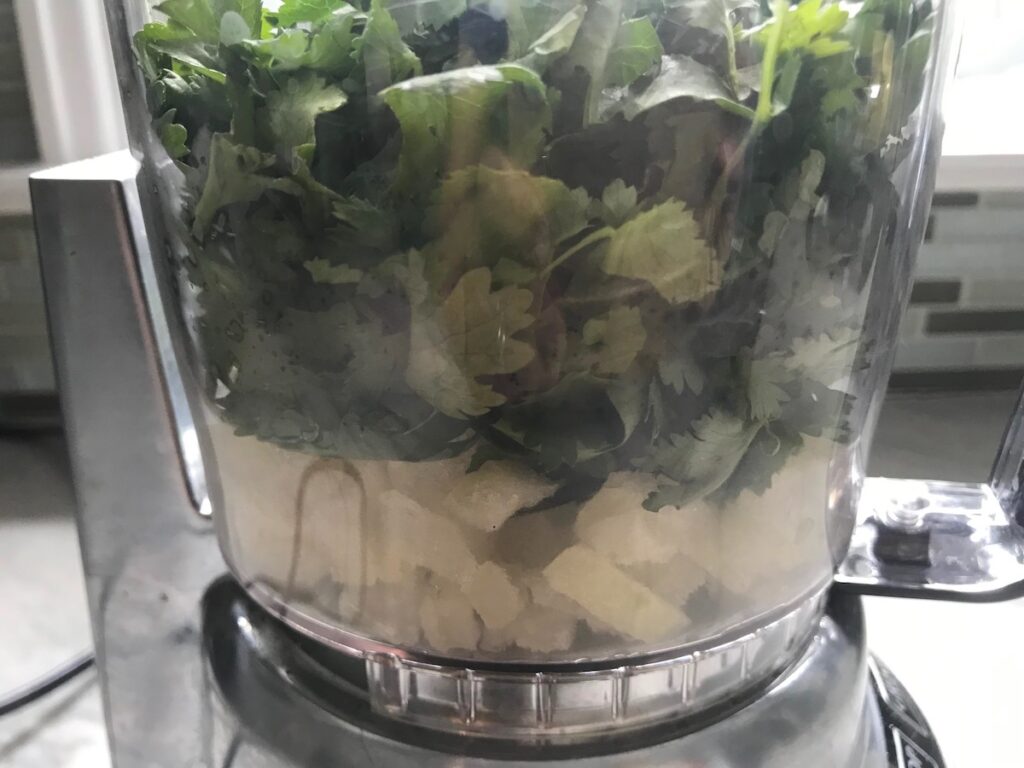 Onion, cilantro, and garlic in food processor for Feijoada recipe. It is rice and beans Brazilian style with pork sausages, beef, and more.