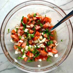 Tomato and onion salad in clear bowl on counter. It has diced tomato, diced onion, basil, and vinegar.