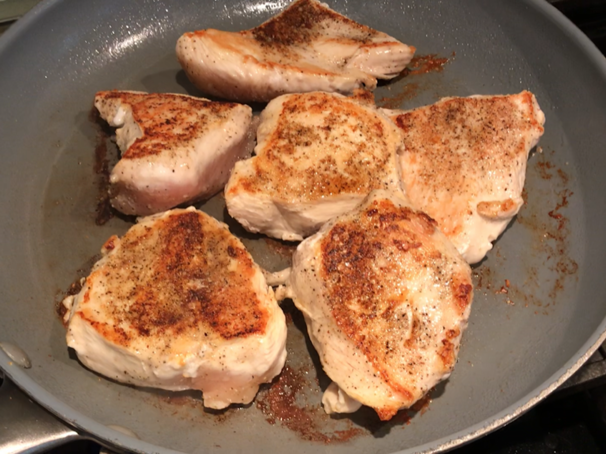 Browned chicken in skillet on stove for Brazilian Chicken in peanut sauce recipe.