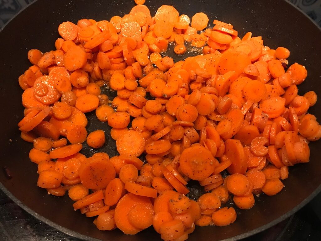 Carrot slices cooking in a skillet for this Carrot Bacon Recipe.