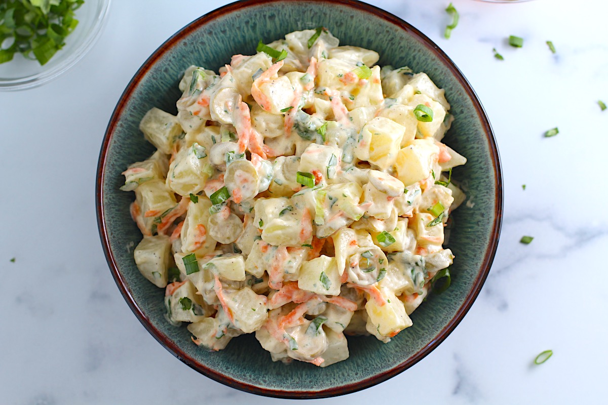 Brazilian Potato Salad in a bowl with carrots, green olives, cilantro, and a mayonnaise dressing, and cilantro garnish on top.