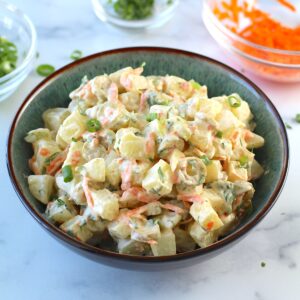 Brazilian Potato Salad in a bowl with carrots, green olives, cilantro, and a mayonnaise dressing, and cilantro garnish on top.