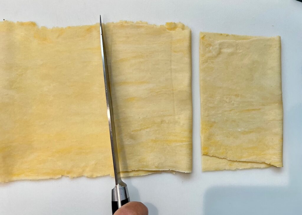 knife cutting squares of dough that have been folded over for Brazilian Pastel recipe.