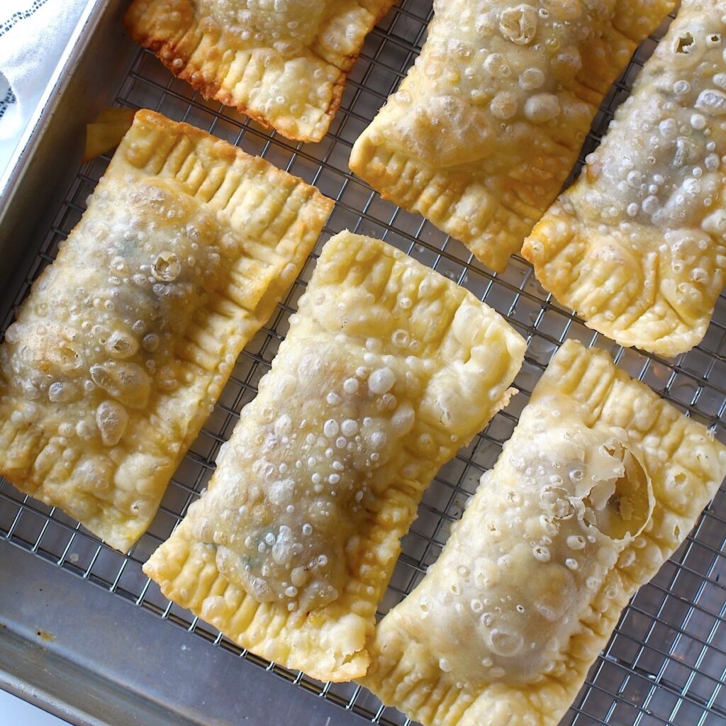 Six golden brown fried Pasteis on rack over sheet pan for traditional Brazilian Pastel Recipe with ground beef filling.