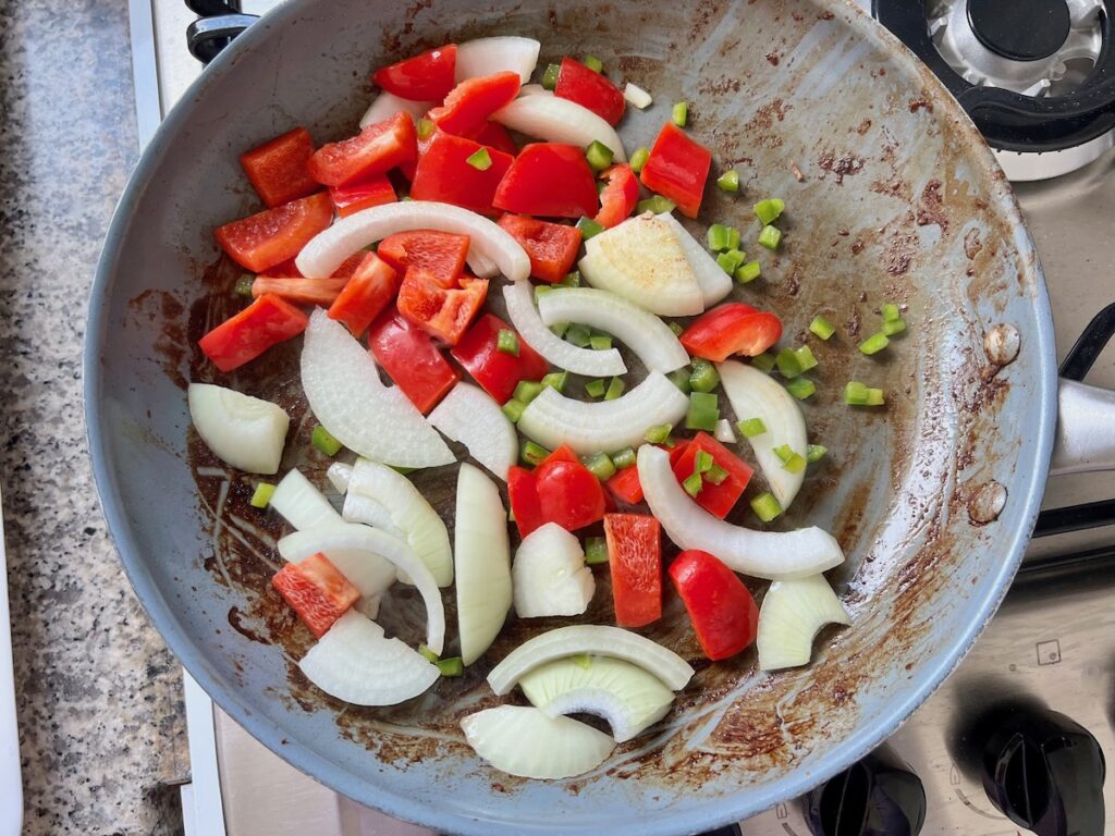 Chopped red pepper, jalapeno, and onions cooking in a skillet on stove for Marinated Chicken Stir Fry recipe.