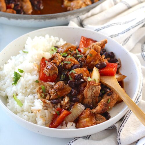 Brazilian Marinated Chicken Stir Fry with pineapple, black beans, red Pepper and onions in a bowl over white rice with a bamboo fork and cilantro garnish. It is truly one amazing dish with incredible flavor!