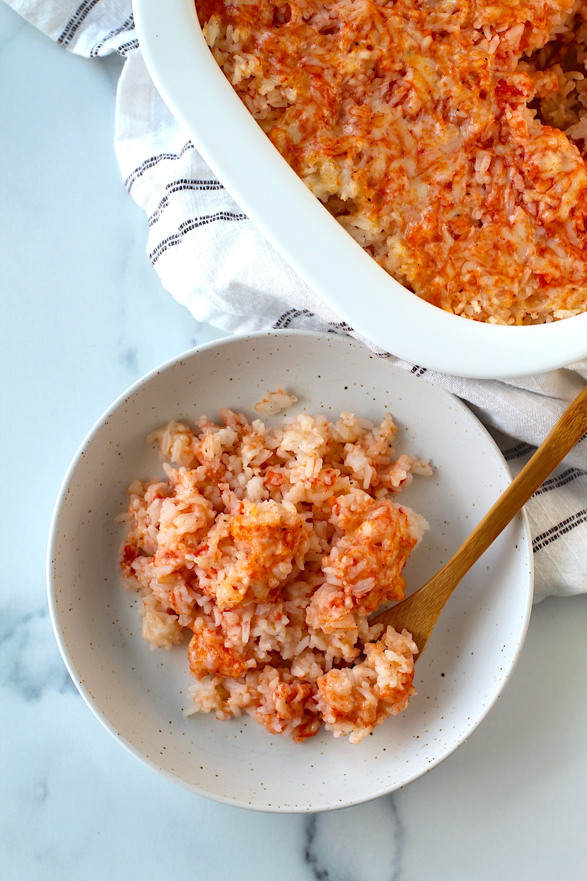 Spoon in bowl of Baked Rice with Cheese and Tomatoes with casserole dish in background.