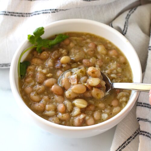 Spoon scooping up Carioca beans from a bowl of beans with cilantro leaves on top.