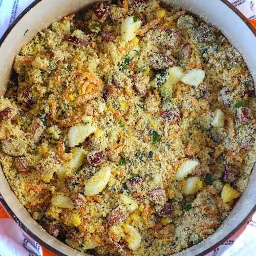 Brazilian Farofa Recipe in a pot on blue and white towel on counter. It has bacon, sausage, green olives, hard boiled eggs, carrots, onions, and garlic and is a delicious traditional recipe for Christmas ~ Farofa de Natal.