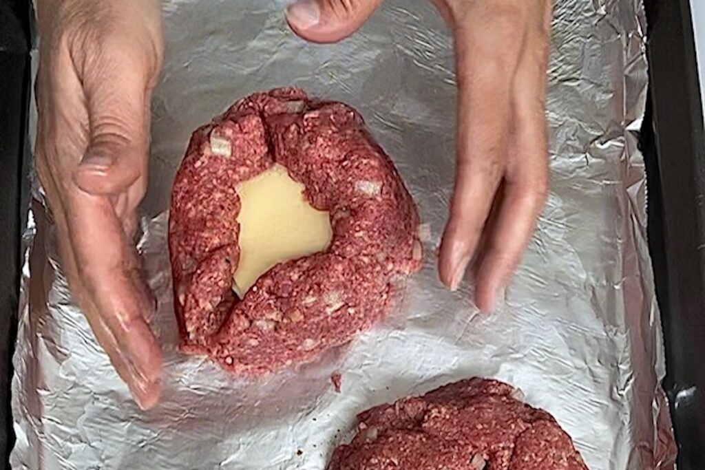 Hands folding sides of beef patty up around the mozzarella cheese to make the polpettone.