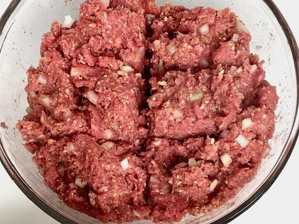 Ground beef mixed with ingredients and divided into 6 sections in q bowl for Polpettone recipe.