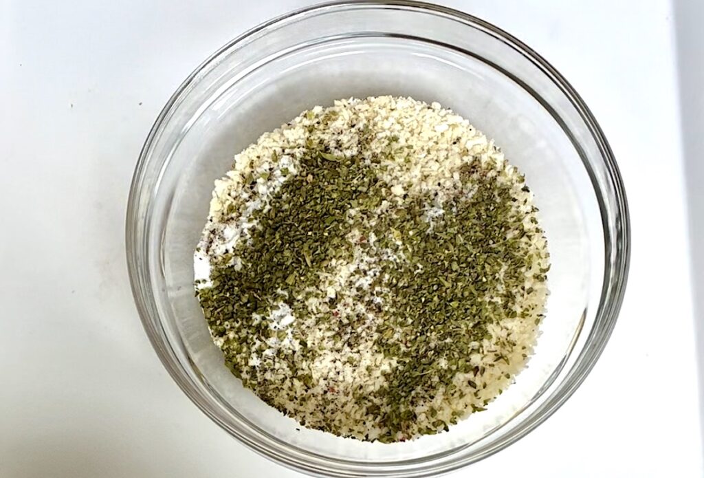 Breadcrumbs, oregano, salt, and pepper in a bowl before being mixed.