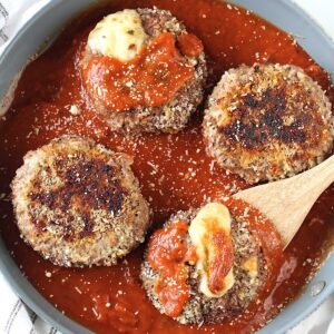 Four Ground beef Polpettone sitting in tomato sauce in a skillet with mozzarella cheese oozing out of a couple of them.