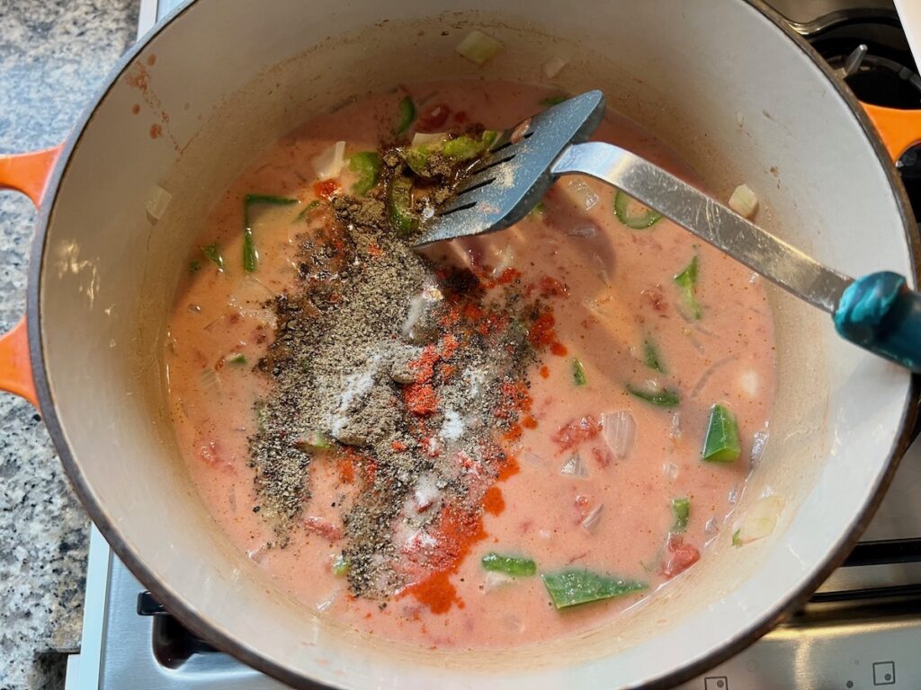 Seasonings add to mixed diced tomatoes, coconut milk, green peppers, onions in a pot for Moqueca de Ovos.