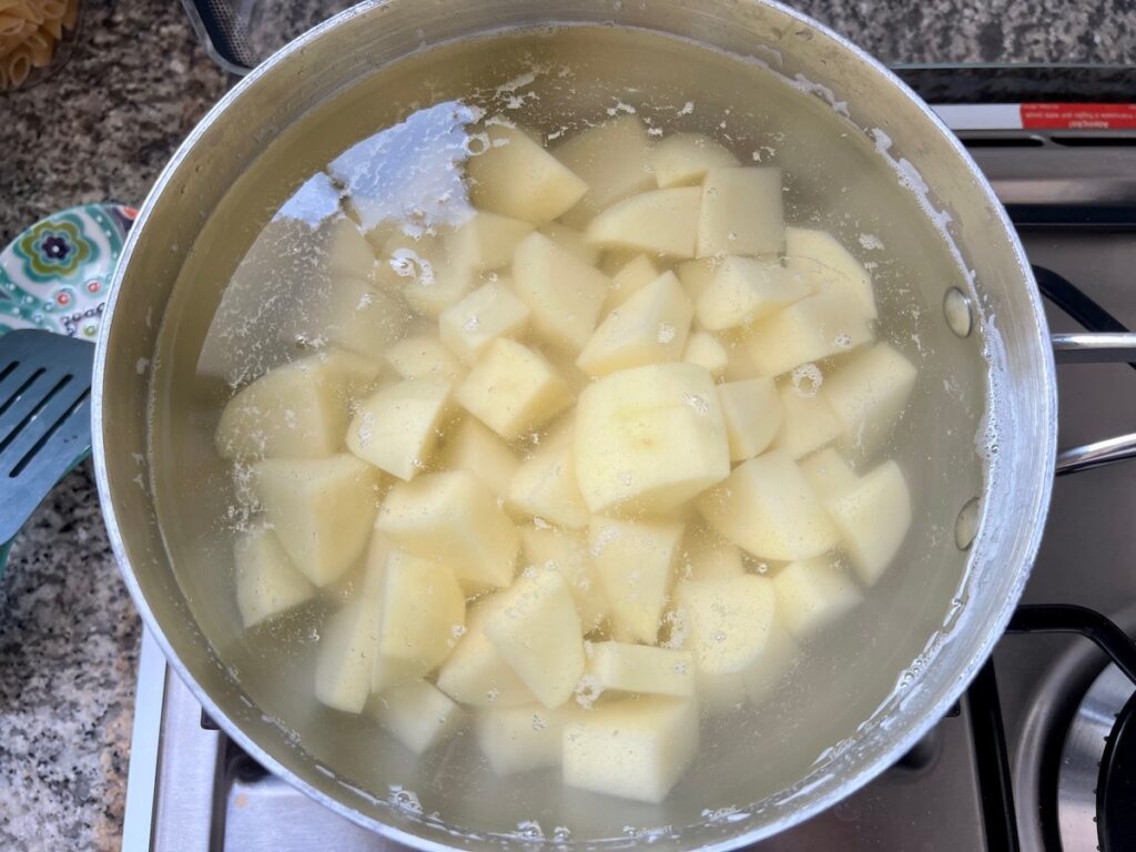 Cut pieces of potato cooking in salted water on stove for Dutch oven Shepherd's Pie.