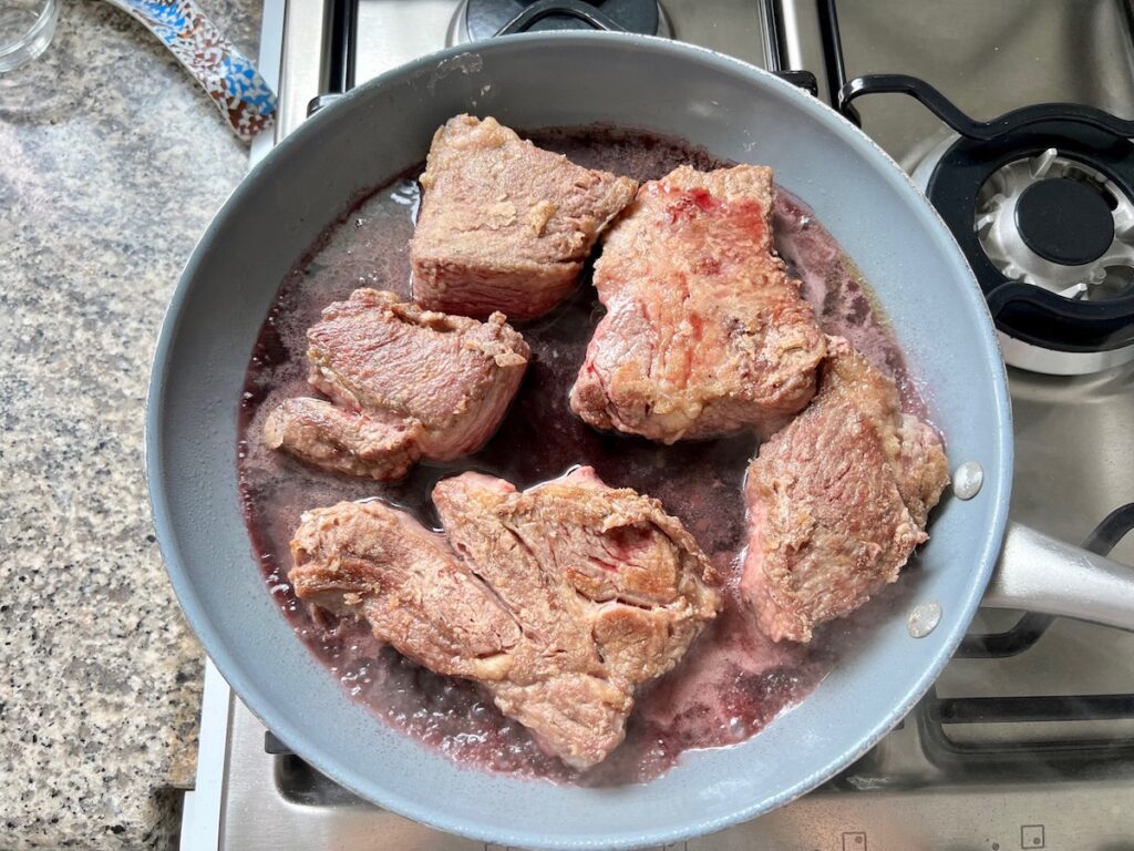 Seared beef ribs and wine in skillet for Brazilian Vaca Atolada Beef Rib Stew.