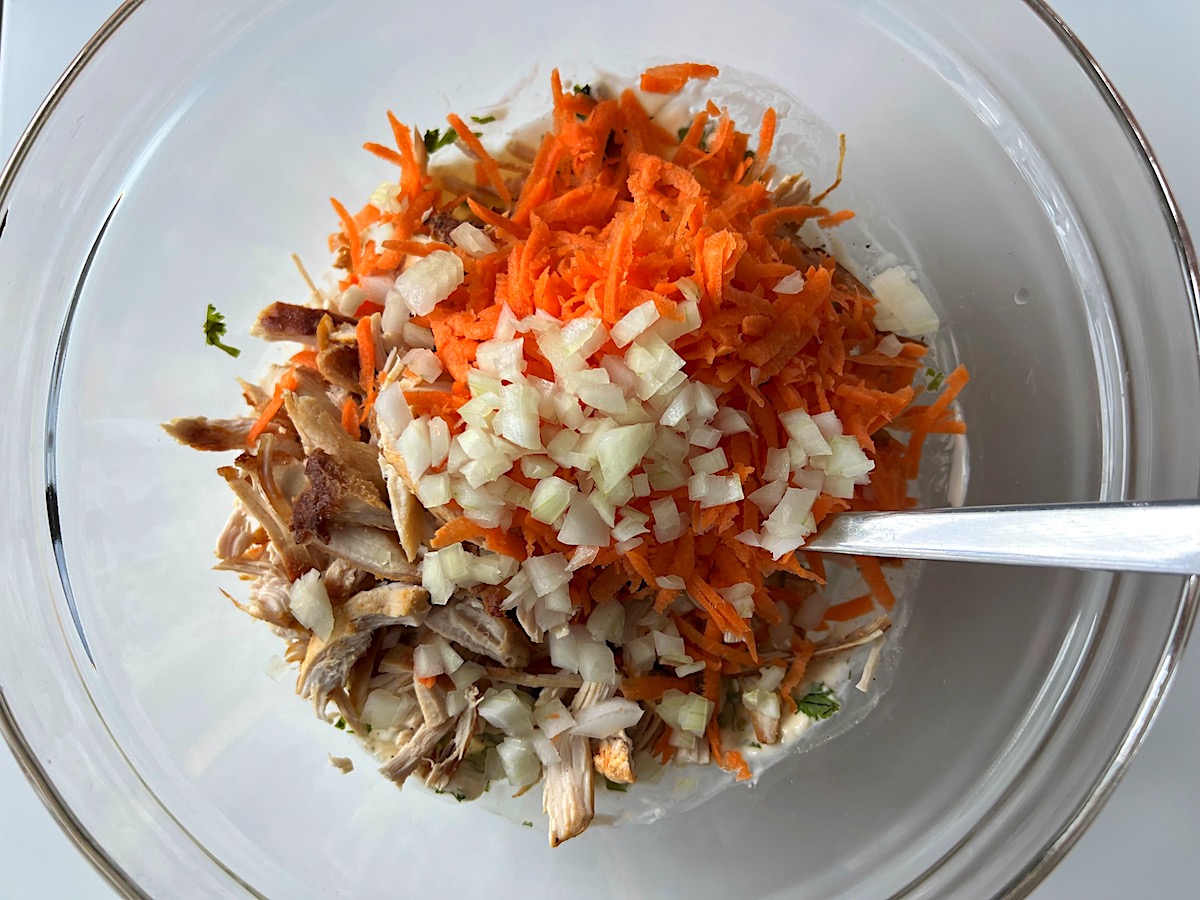 Bowl with mayonnaise dressing, shredded chicken, carrots, and onion before being mixed for Brazilian Chicken Salad. 
