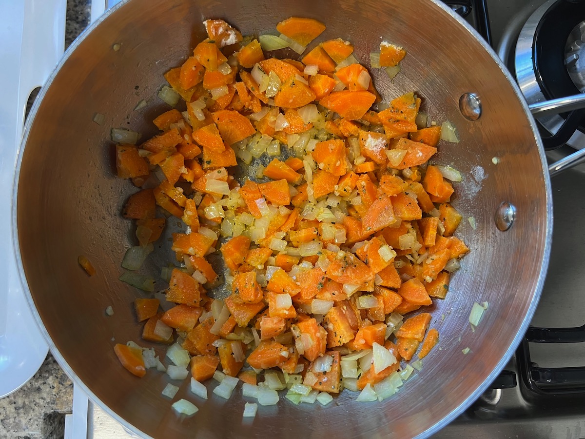 Flour and oregano mixed into diced carrots, onions, and minced garlic in a pot cooking for Carrot Sauce.