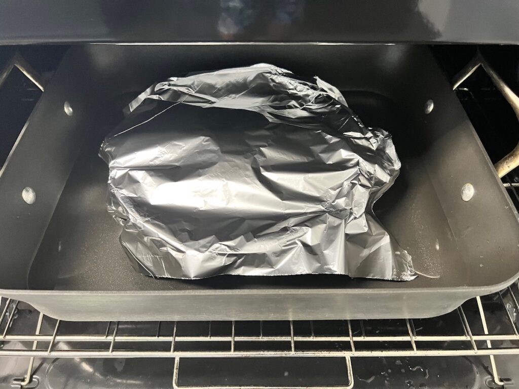 Flan pan covered with aluminum foil in water bath in oven.