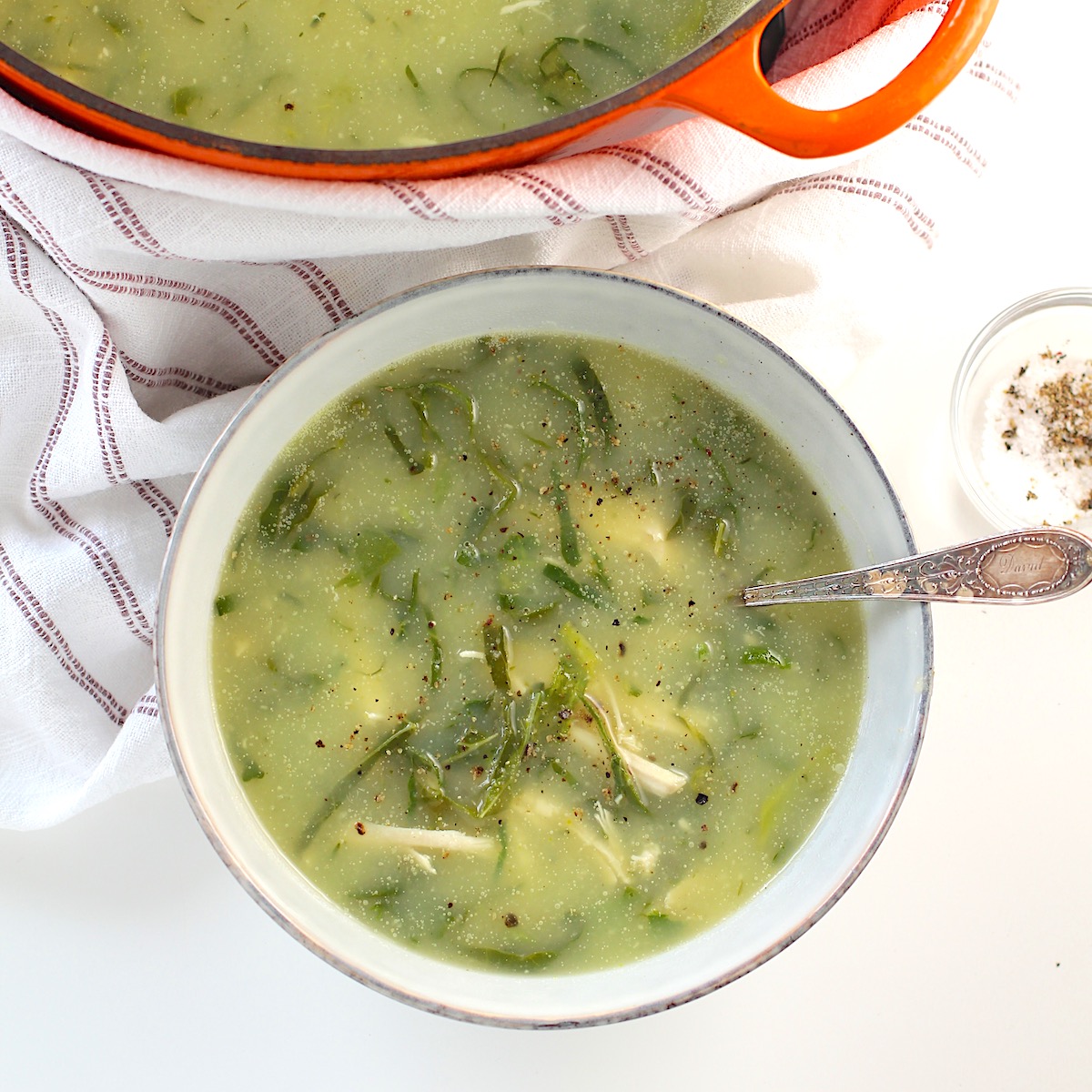 Chicken Kale Soup thickened with pureed potatoes (Caldo Verde com Frango) in a bowl with spoon on table with pot of soup in the background.
