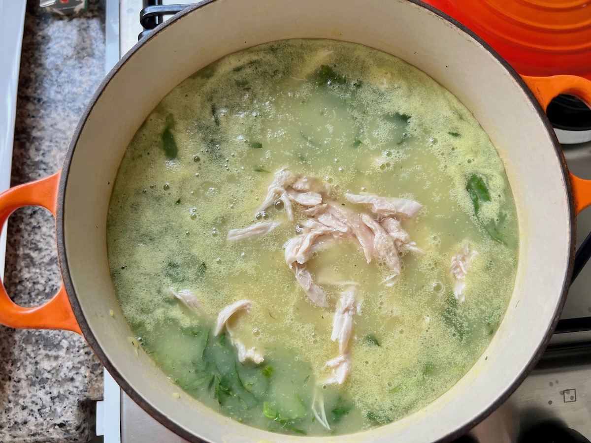 Shredded chicken added to Chicken Kale Soup thickened with pureed potatoes (Caldo Verde com Frango) in a pot on stove.