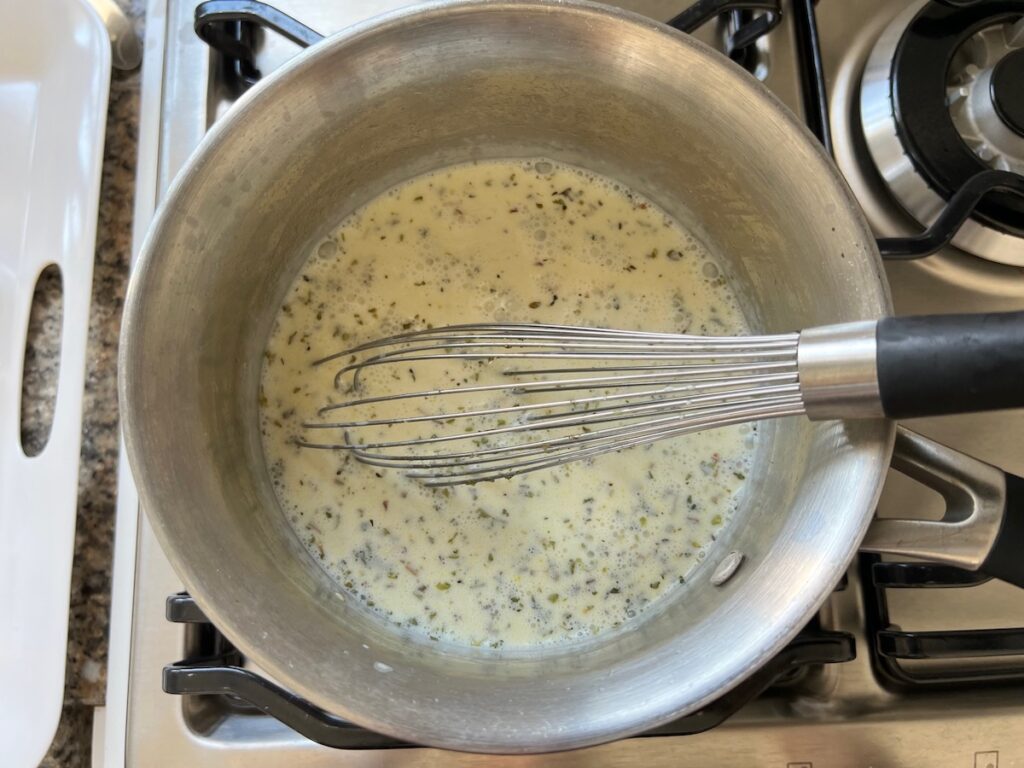 Heavy cream and oregano added to butter and garlic cooking in a saucepan for Spicy Sausage Pasta.