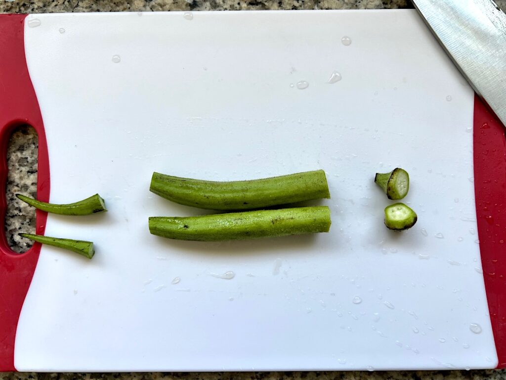 Fresh okra on a cutting board with stem end cut off and small end cut off.