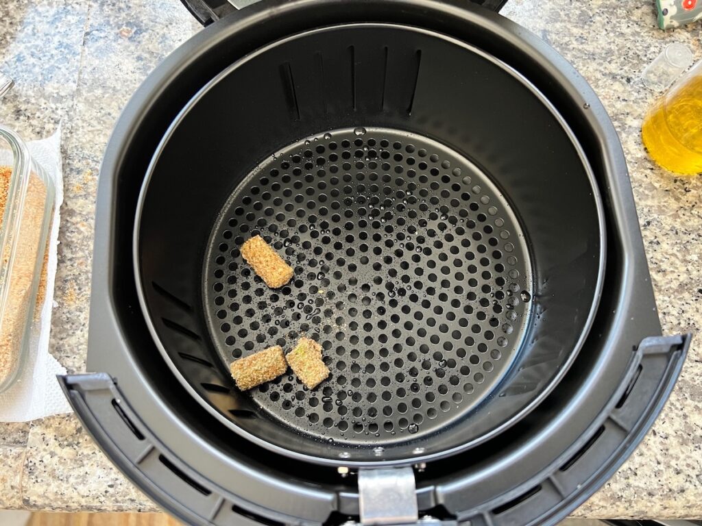 Air fryer basket sprayed with oil and starting to put 3 breaded okra into the basket for Breaded Okra in air fryer.