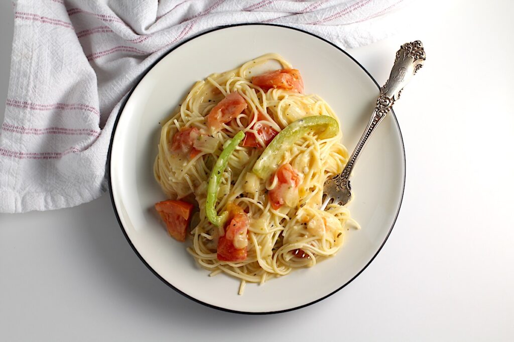 Coconut Milk Pasta Sauce with tomatoes and green pepper mixed with spaghetti pasta on a plate with fork holding a bite of pasta.