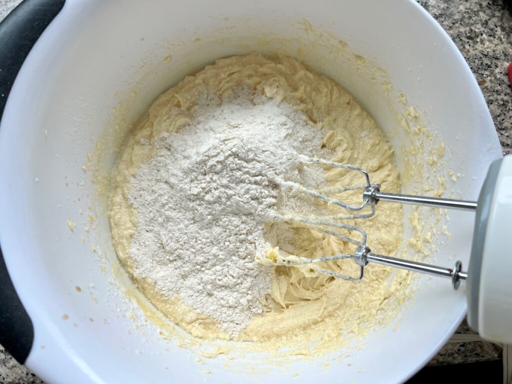 Flour added to batter in a bowl with hand mixer pulled out for Orange Bundt Cake recipe.