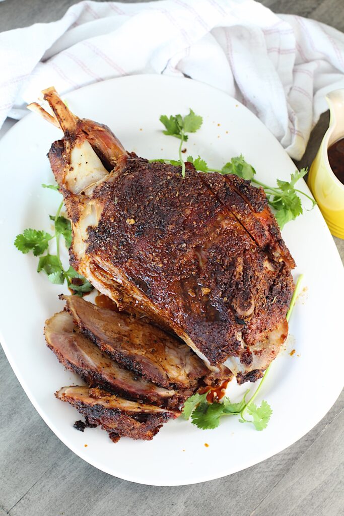 Whole roasted pork shoulder on the bone on a platter with some of it sliced for the Pork shoulder brine recipe.