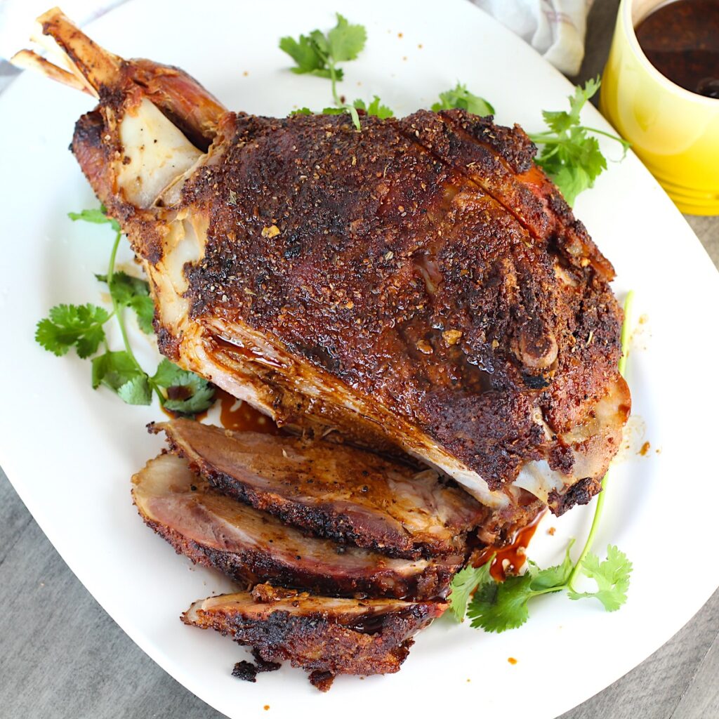Whole roasted pork shoulder on the bone on a platter with some of it sliced for the Pork shoulder brine recipe.