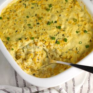 Corn Casserole Recipe with Cream Cheese and scallion slices on top in casserole dish with a spoon scooping some from the corner.