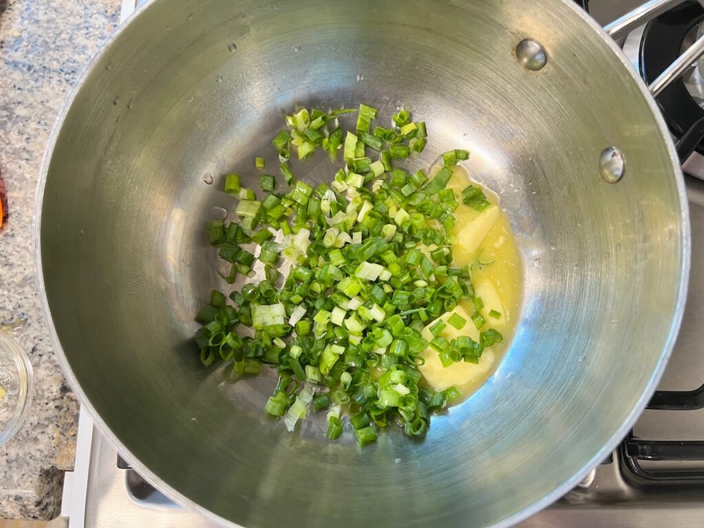 Butter and scallions in a pot on stove to cook for Corn Casserole Recipe with Cream Cheese.