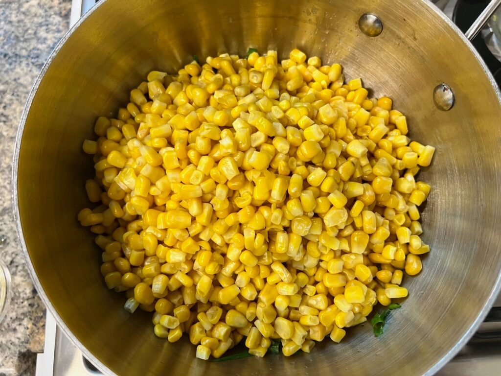 Corn added to pot with scallions and butter for Corn Casserole Recipe with Cream Cheese.